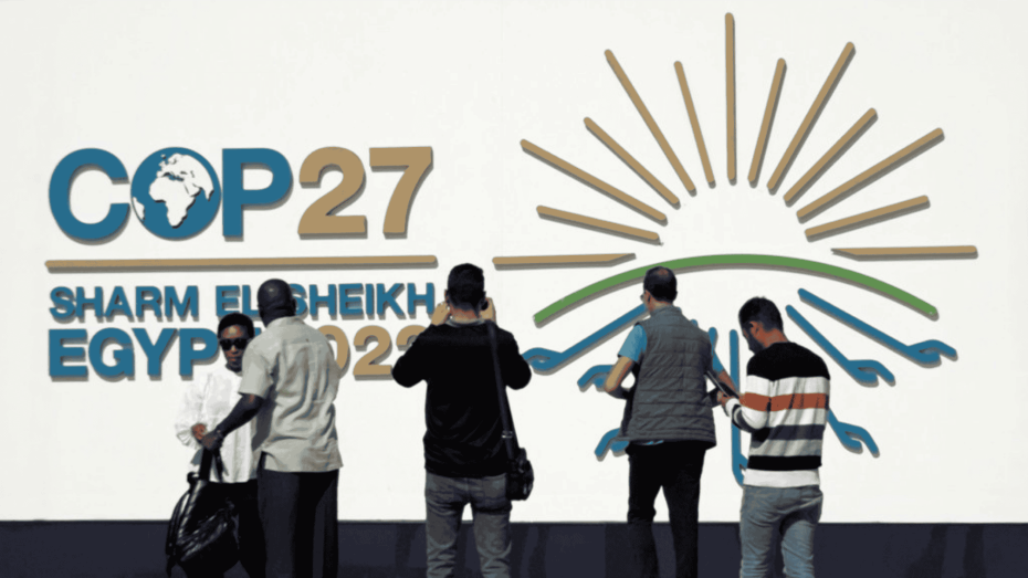 مجموعة من الحاضرين يقفون أمام شعار مؤتمر الأمم المتحدة للمناخ COP27 في مدينة شرم الشيخ المصرية.