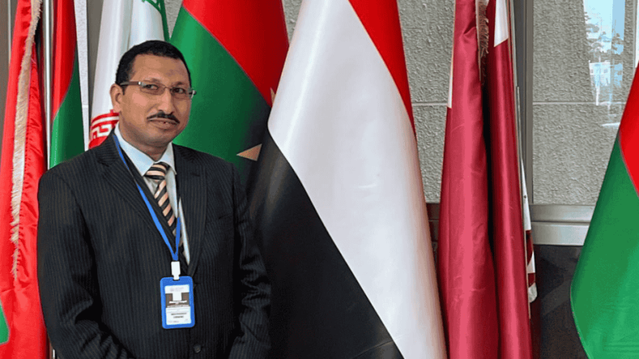 محمود جابر أمام أعلام الدول المشاركة في الدورة الـ85 للجنة الإفريقية لحقوق الإنسان والشعوب.