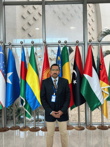 مشاركة عدالة ضمن وفود الدورة الإفريقية لحقوق الإنسان – بانجول محمود جابر أمام أعلام الدول العربية والإفريقية المشاركة في الدورة الـ85.