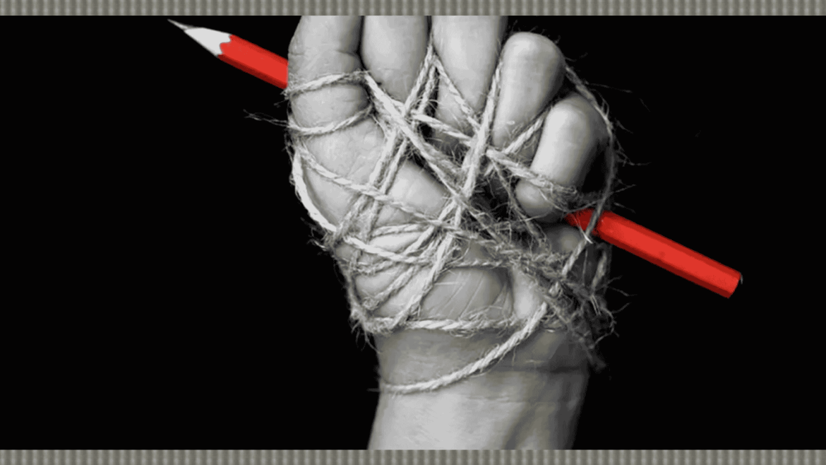 يد مقيّدة بالحبال تمسك قلمًا أحمر في مشهد يرمز لقمع حرية الصحافة والتعبير.