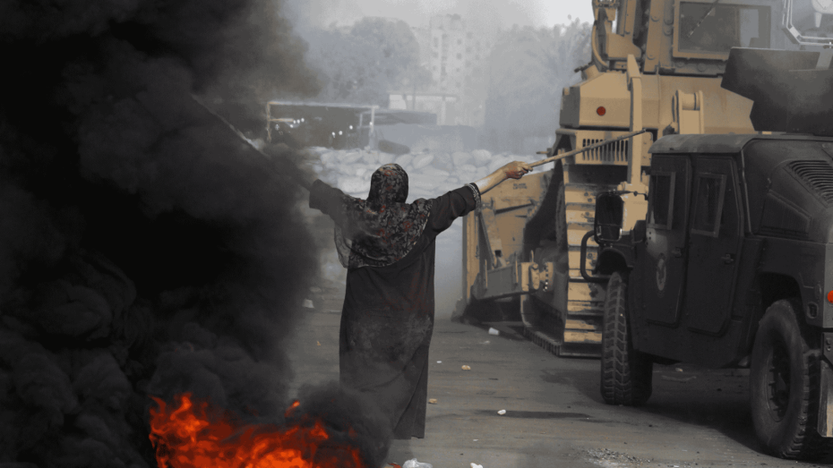 امرأة مصرية تقف بيدين مرفوعتين أمام مدرعات وقوات أمن خلال فض اعتصام رابعة وسط دخان كثيف وحرائق.