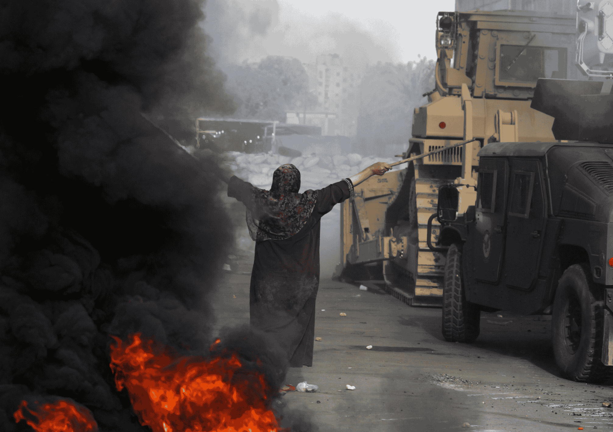 امرأة مصرية تقف بيدين مرفوعتين أمام مدرعات وقوات أمن خلال فض اعتصام رابعة وسط دخان كثيف وحرائق.