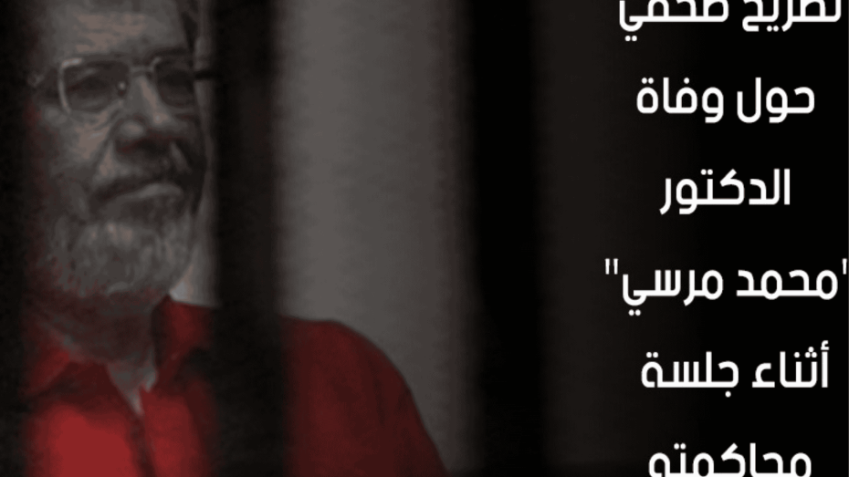 الرئيس المصري الراحل محمد مرسي داخل قفص المحكمة، مرتديًا ملابس الاحتجاز الحمراء، مع ظهور حواجز حديدية أمامه، في مشهد يعكس ظروف محاكمته القاسية.