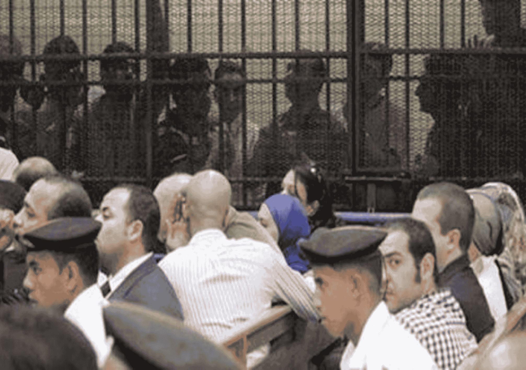 صورة من داخل قاعة محكمة مصرية تُظهر متهمين يجلسون داخل قفص الاتهام الحديدي، وخلفهم حراسة مشددة من قوات الأمن، في مشهد يعكس واقع المحاكمات الجماعية في مصر.
